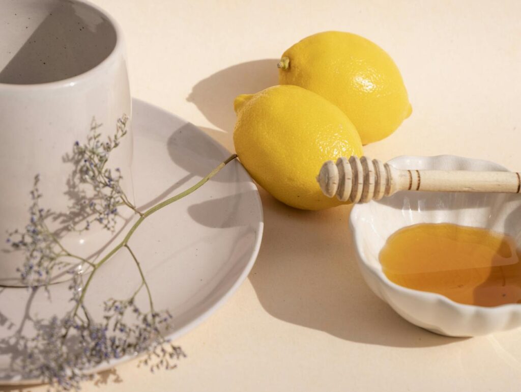 Minimalist setup featuring a ceramic cup, lemons, and honey on a flat surface.